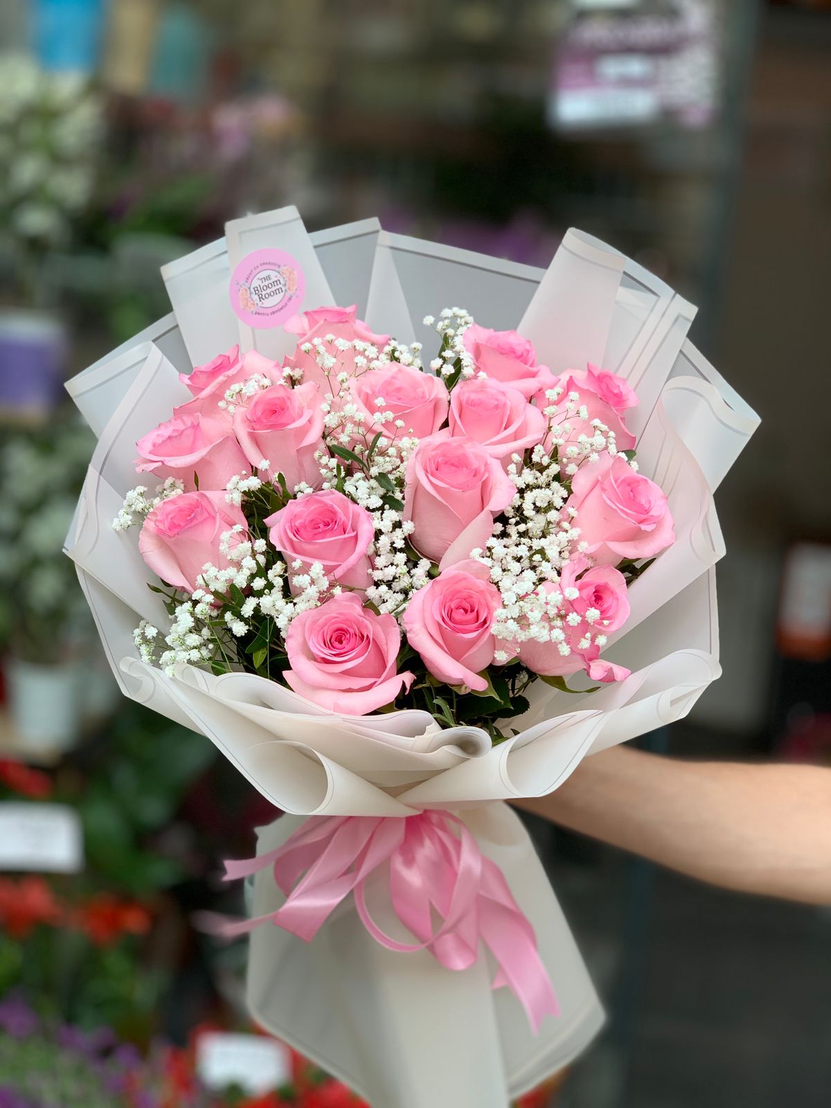 Buchet romantic cu 15 trandafiri roz proaspeți și gypsophila albă și pistachio verde, înfășurat elegant în hârtie crem cu fundă roz.